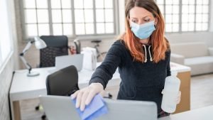 Woman wearing mask cleaning laptop at the office